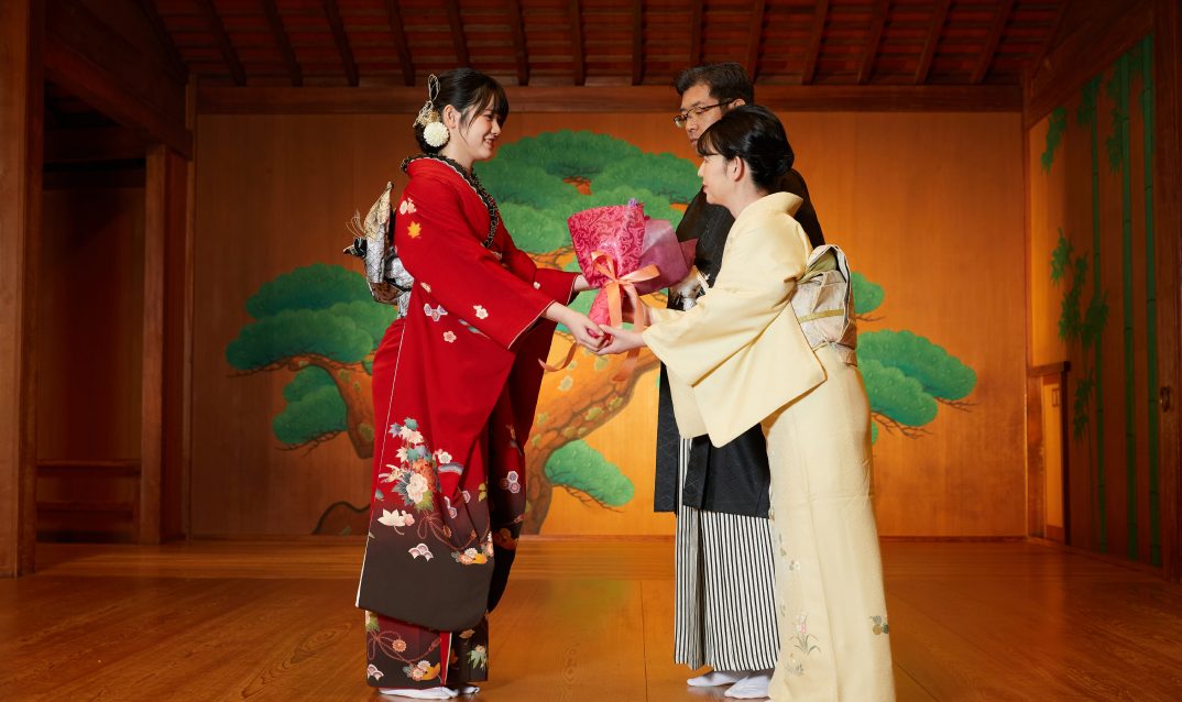 晴れ着姿で贈り物を渡す新成人と家族
