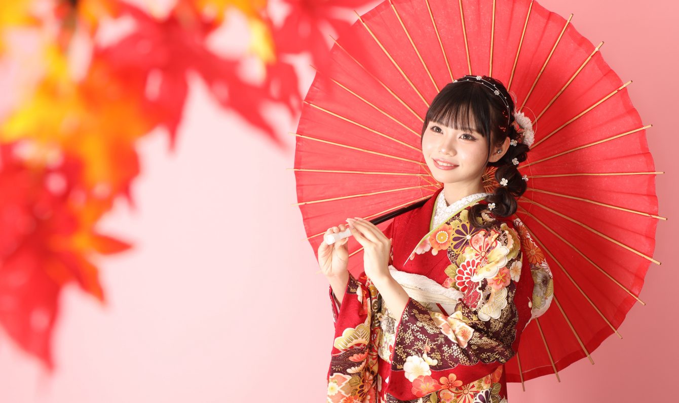 紅葉を背景に赤い和傘を持つ振袖姿の新成人